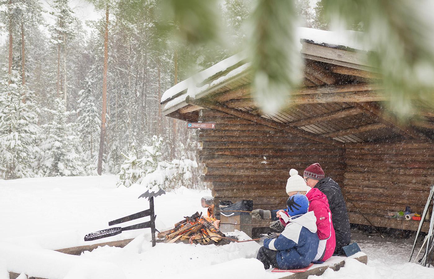 Perhe istumassa laavun suojassa Kyrkösjärven luontoreitillä lämmitellen nuotion äärellä.