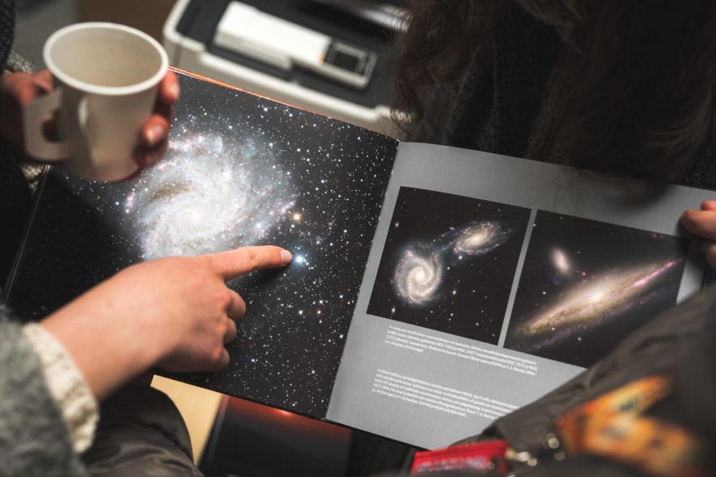 Nainen osoittee avaruudesta kertovan kirjan kuvaa kahvikuppi kädessään