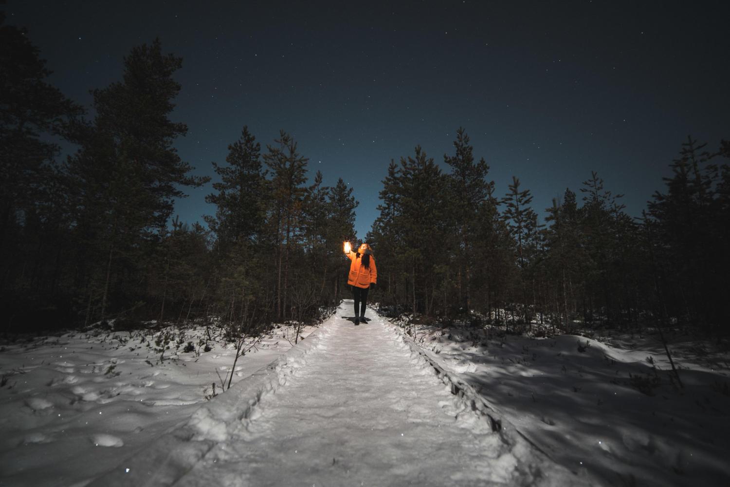 Nainen kävelee kävelyjuntulla lyhty kädessään talvella pimeässä