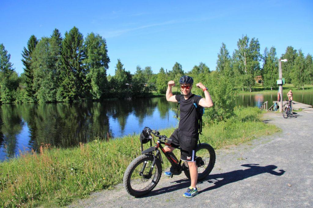 Mies näyttää hauista pyörän päällä, pyörätiellä järven vieressä