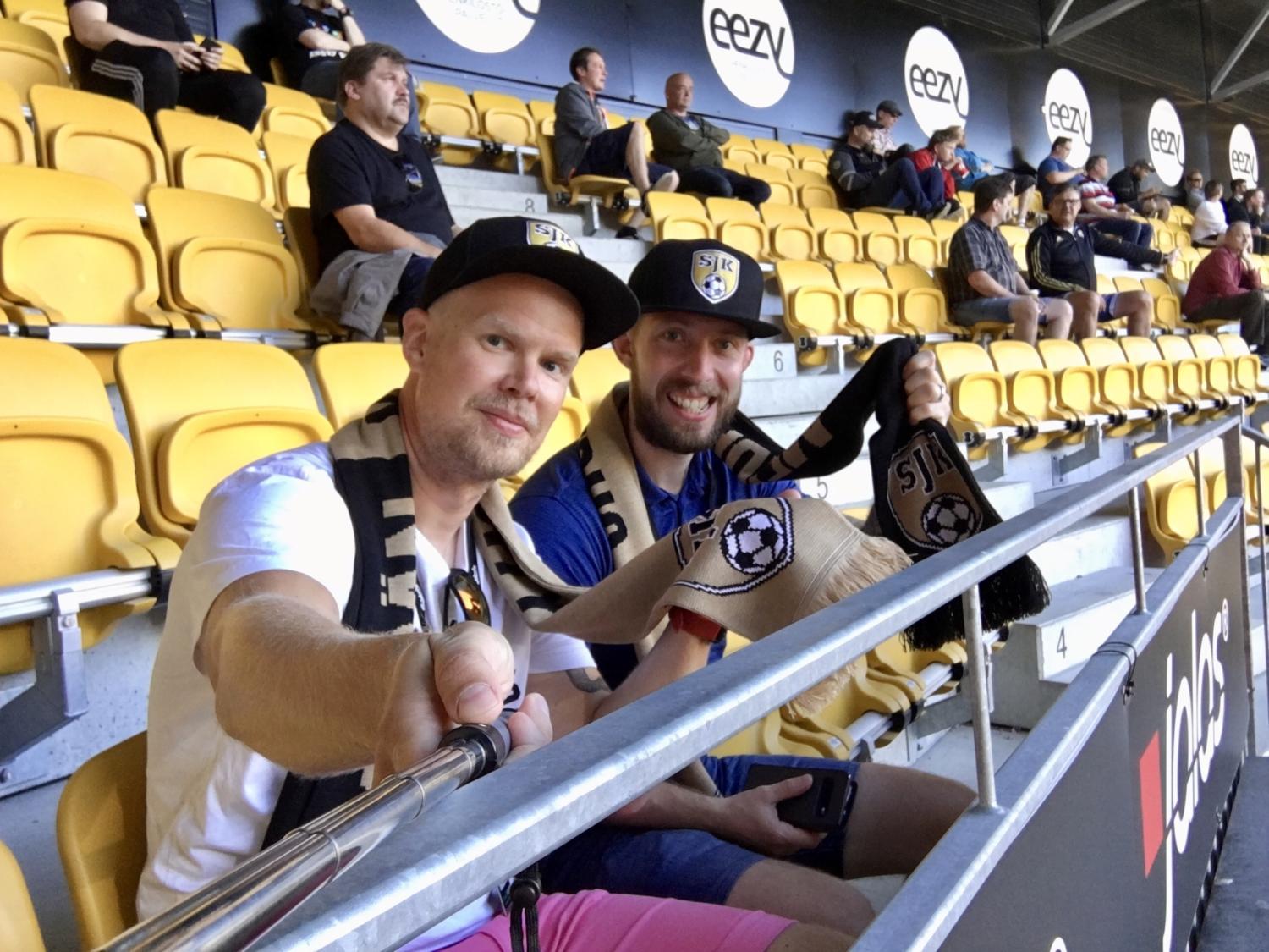 Kaksi SJK-jalkapallo fania ottamassa selfien OmaSp Stadionin katsomon penkeillä