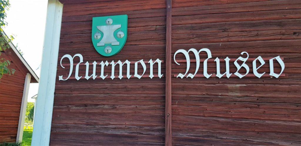 Kyltti, jossa lukee Nurmon Museo ja entisen kunnan vaakuna ripustettuna latoon.