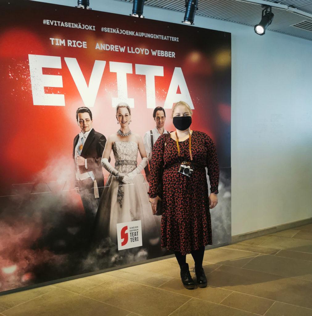Nainen Evita näytelmän ison seinäjulisteen edessä poseeraamassa