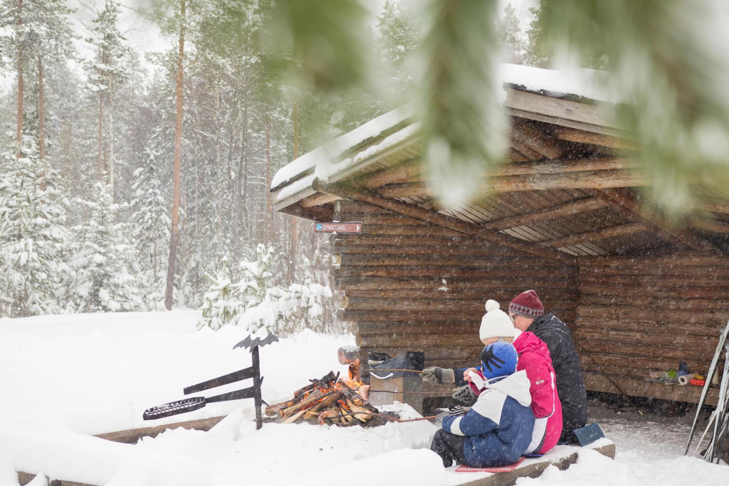Lapsi ja äiti istuvat talvisella laavulla eväiden kanssa.