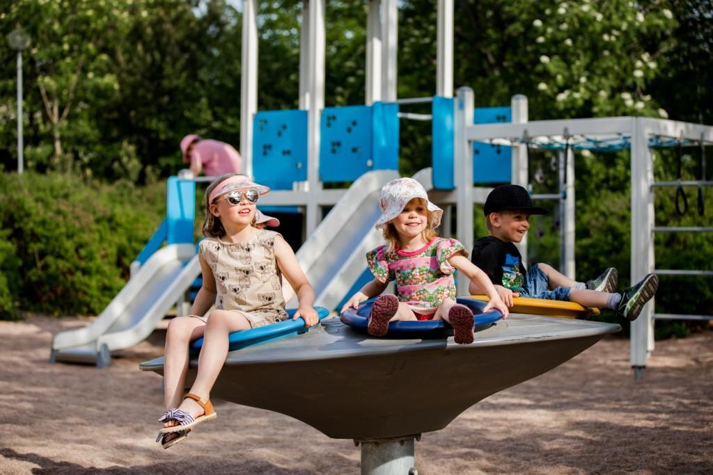 Hymyilevät lapset keskustan pyörivän karusellin päällä leikkipuistossa.