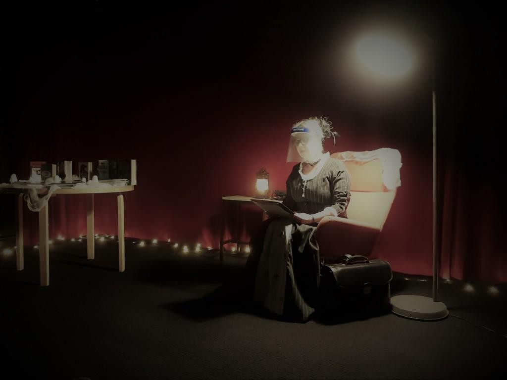 Tarinankertoja lukee tuolilla kummitustarinoita visiiri ja vanhanajan mekko yllään.