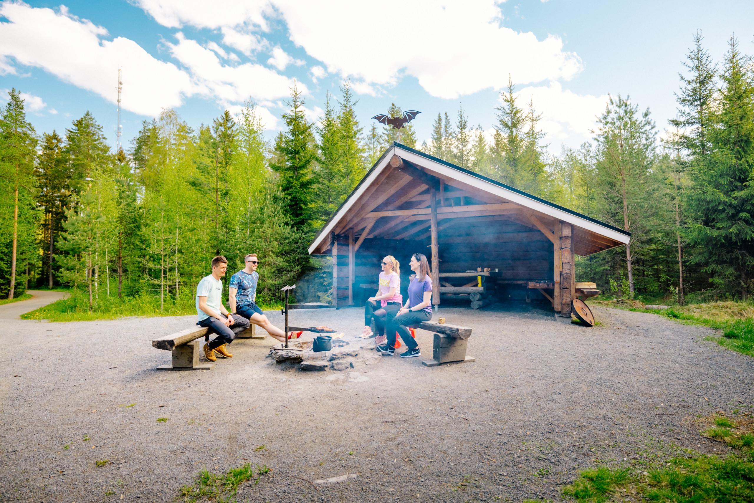 Retkiryhmä laavun edessä syömässä, metsäaukialla.