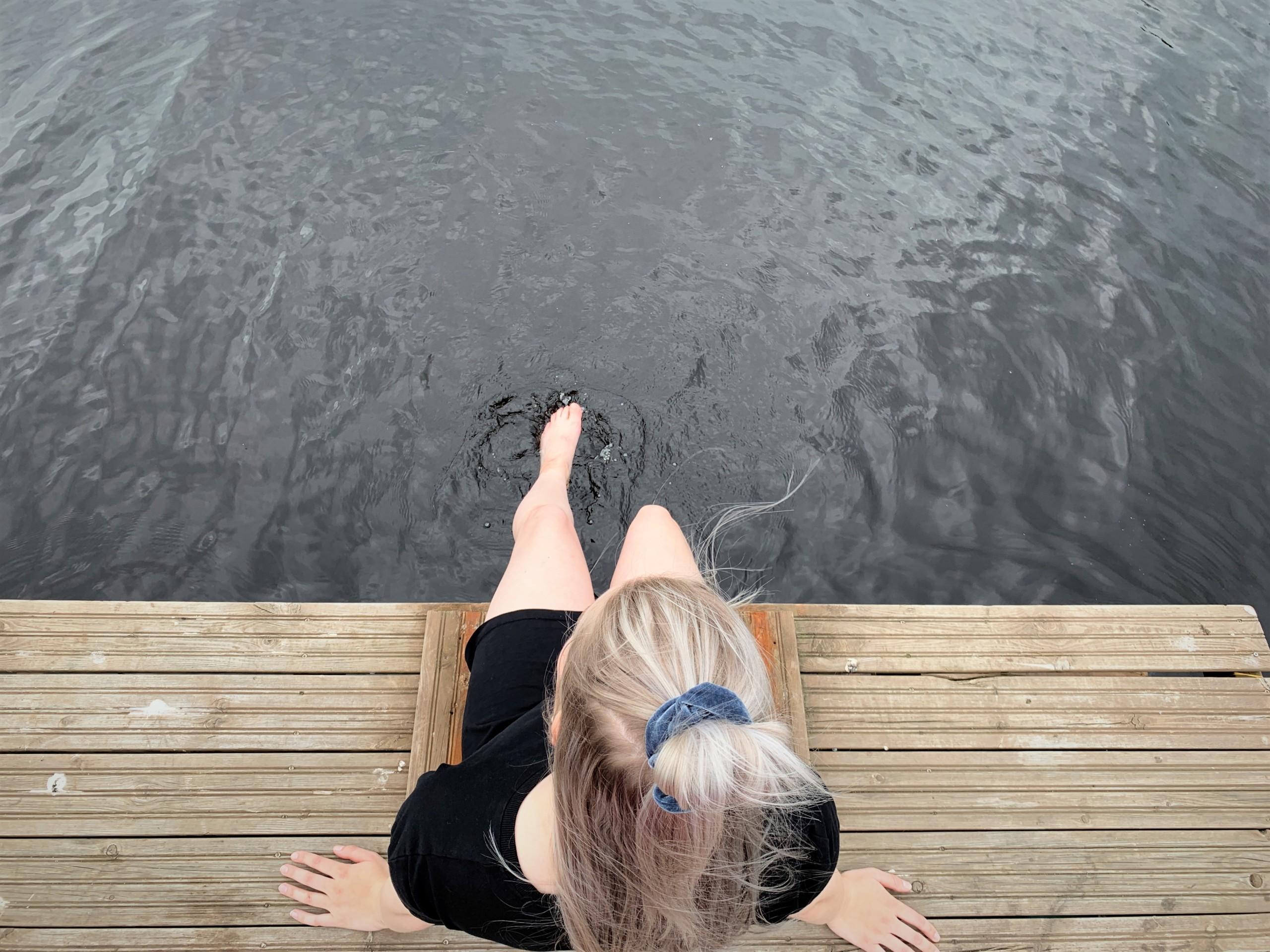 Nainen jalat järvessä laiturin nokassa