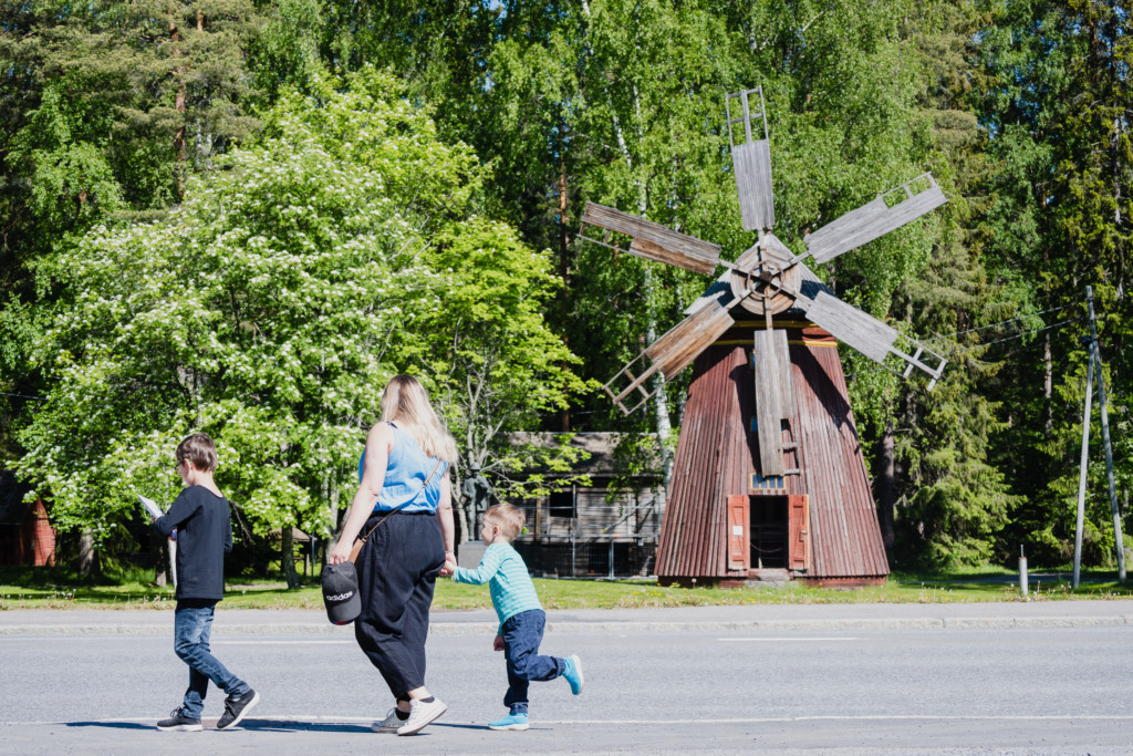 Äiti ja kaksi poikaa kulkevat käsi kädessä Törnävän museoalueen tuulimyllyn ohi