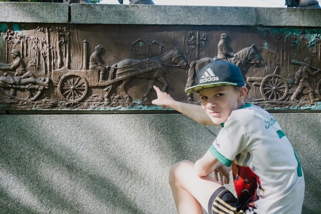 Poika osoittaa kuviointeja Suomenhevonen patsaan jalustan kyljessä
