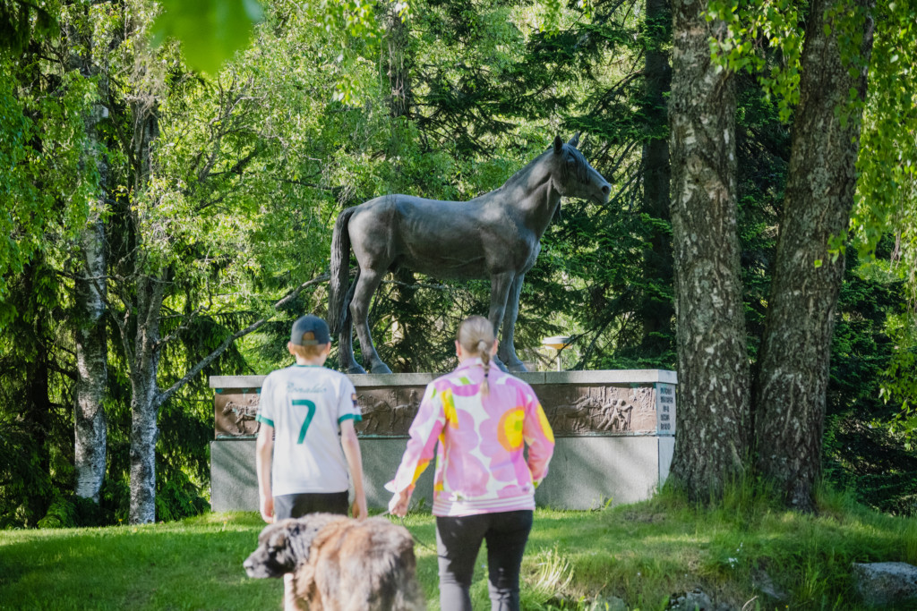 Äiti, poika ja koira kävelemässä kohti Suomenhevonen patsasta kesällä