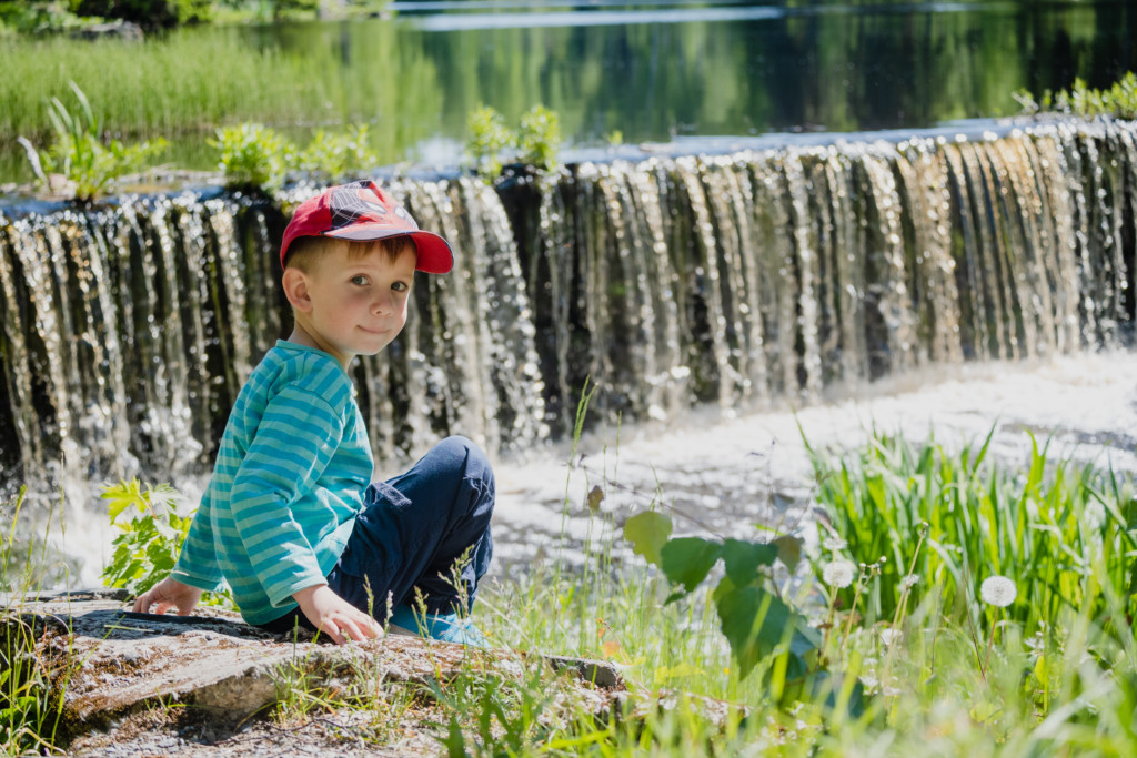 Pieni poika katsoo kameraa istuessaan nurmikolla Törnävän vesiputouksen edessä