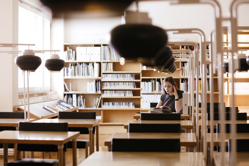 Opiskelija lukemassa Seinäjoen Aalto-kirjastossa Aallon suunnitteleman mustikkalampun alla