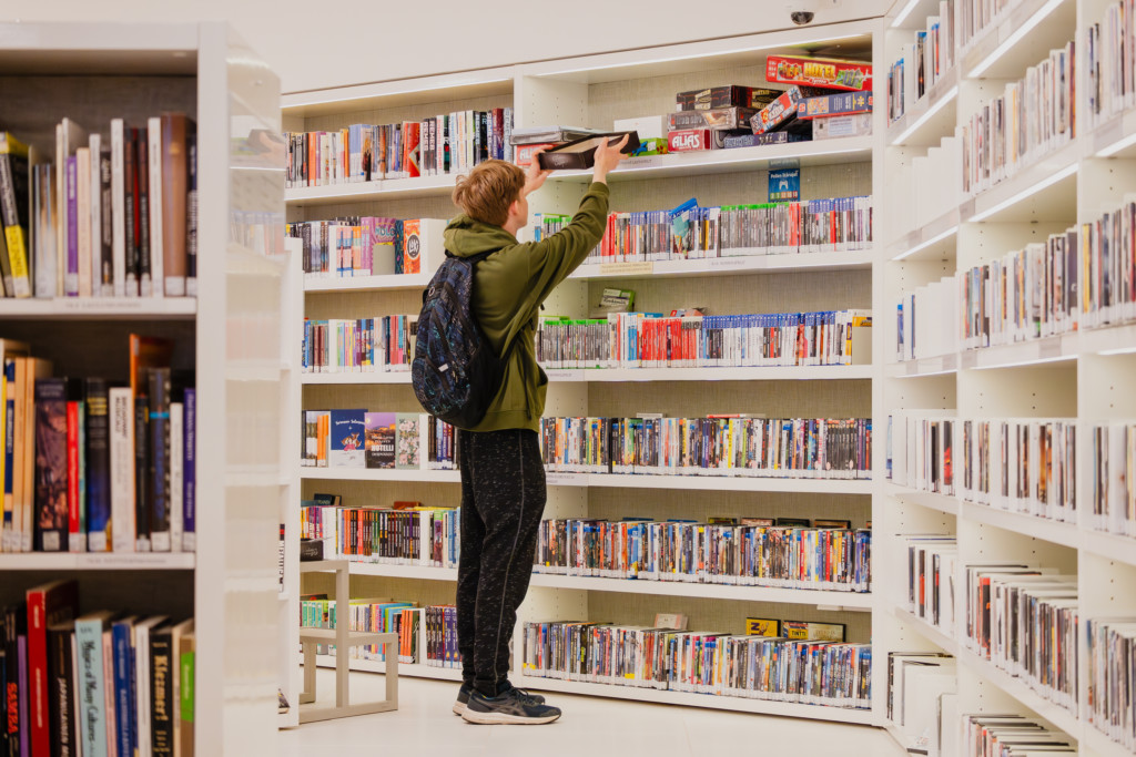 Poika etsii pelejä kirjaston hyllyltä