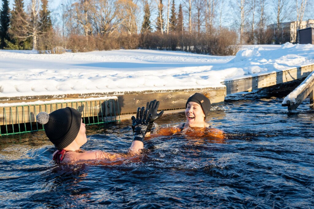 Two women swimming in icy lake with gloves and beanie on