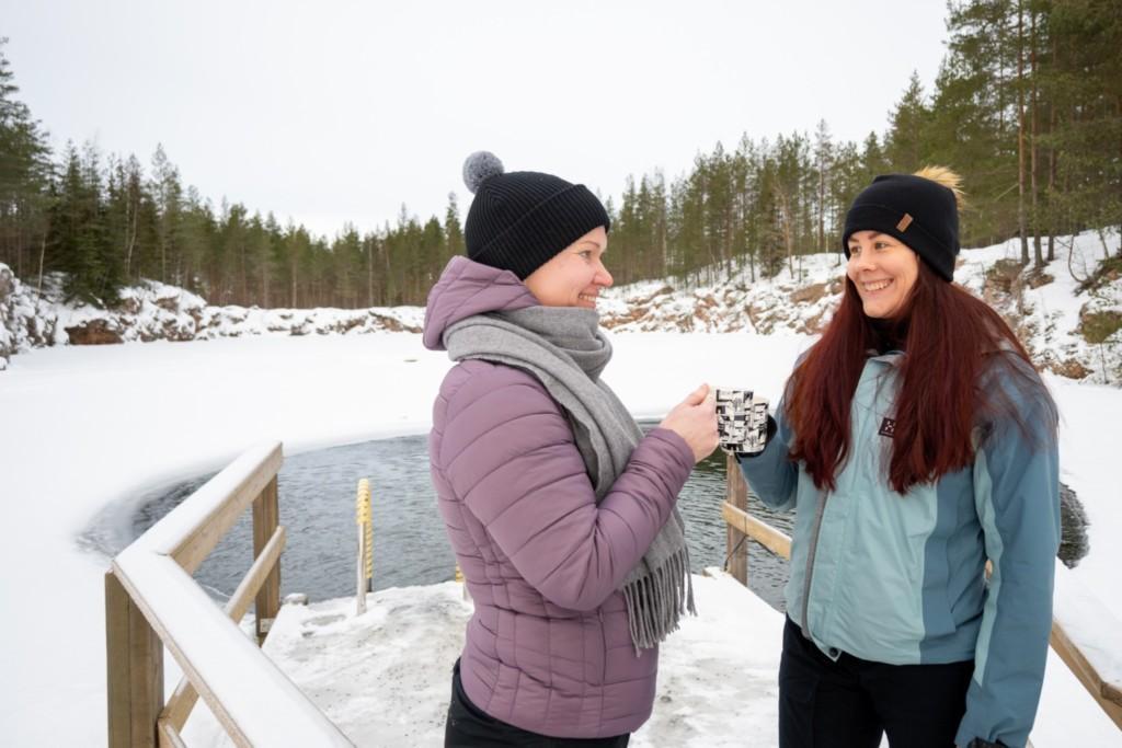 Two women in winter clothing enjoying hot drinks besides frozen lake in Seinäjoki Finland